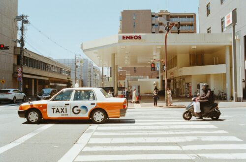 A taxi and scooter cross a zebra crossing.